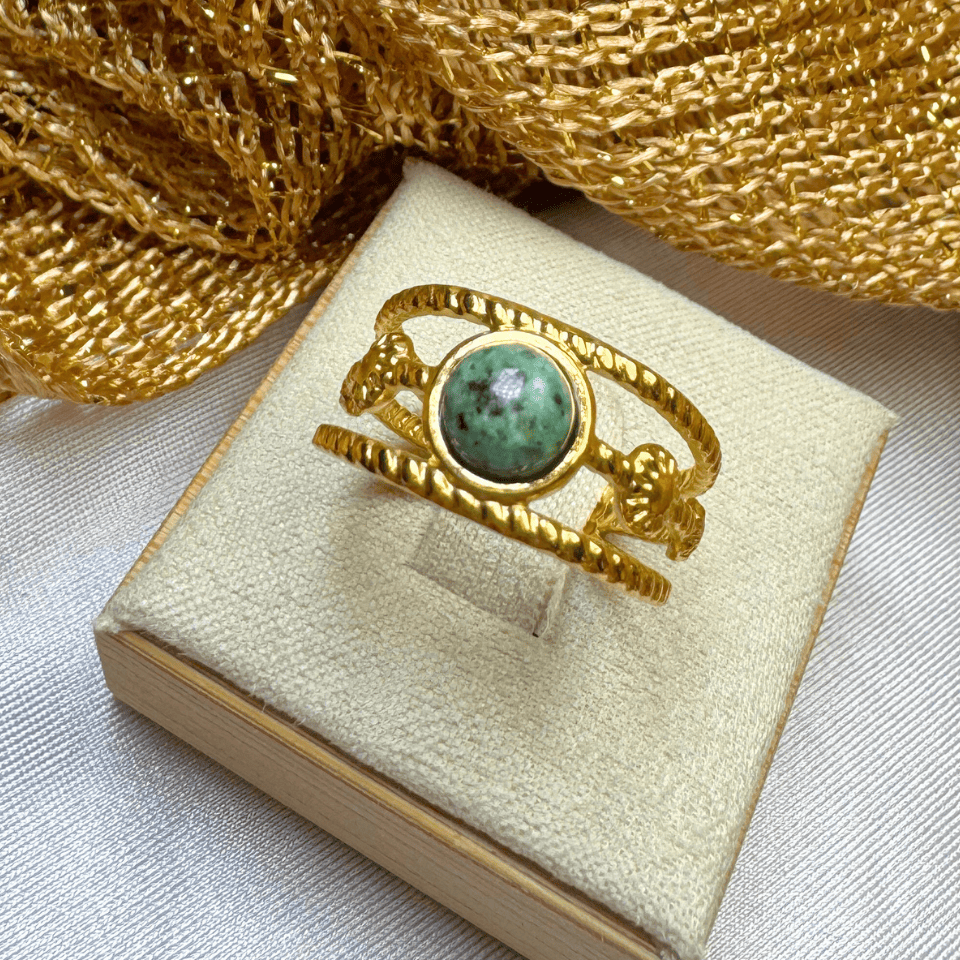 Gold ring with a green gemstone in a jewelry box on a textured gold fabric background