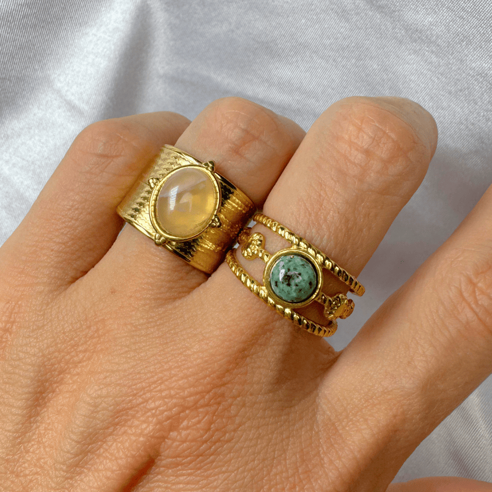 Hand wearing two gold rings with gemstones on a light gray background