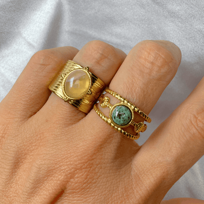 Hand wearing two gold rings with gemstones on a light gray background