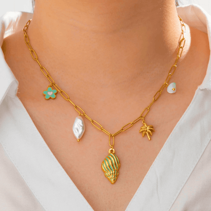 Gold chain necklace with shell and leaf pendants worn by a person in a white shirt.