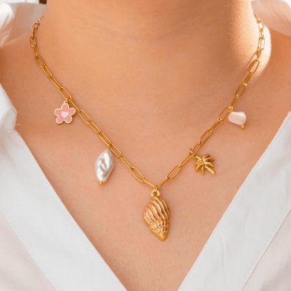 Gold chain necklace with various pendants on a person wearing a white top.