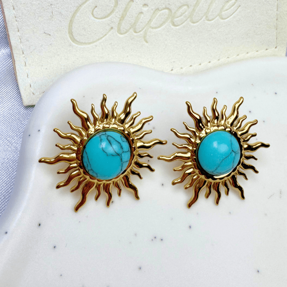 Gold sun-shaped earrings with turquoise centers on a white surface, branded 'Clipette'.