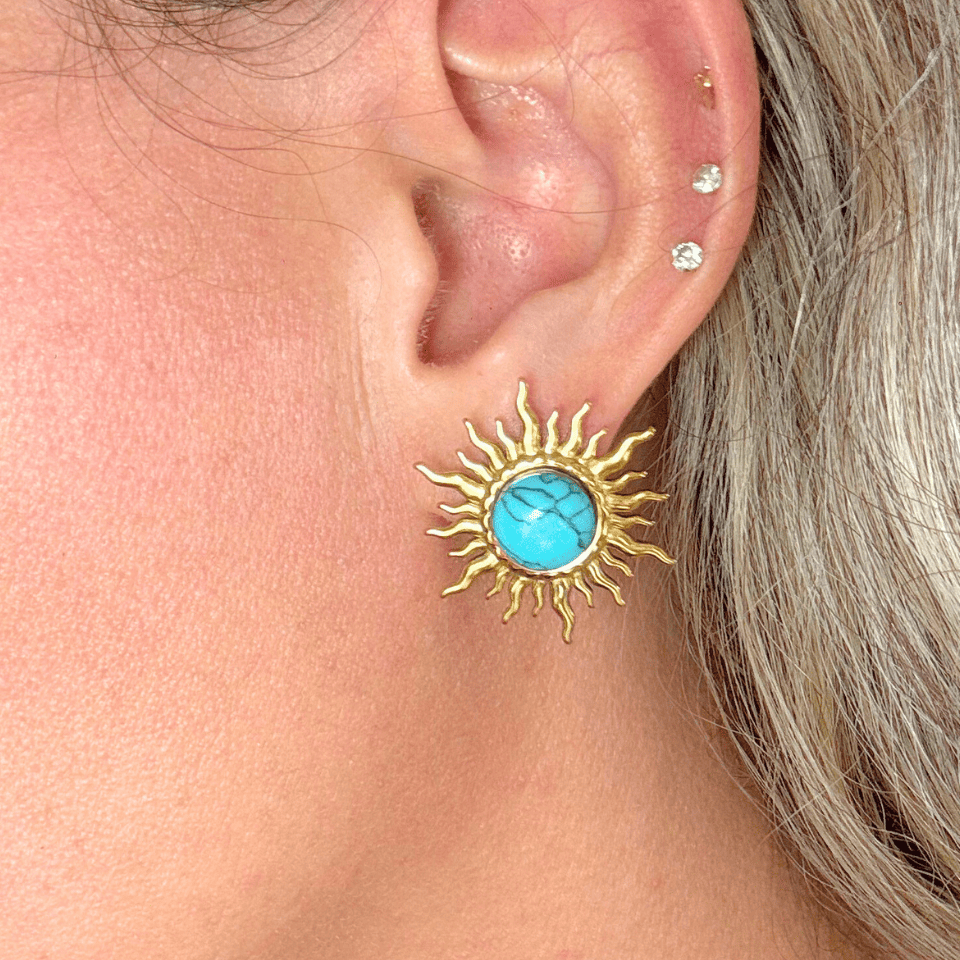 Gold sun-shaped earring with turquoise center worn by a person.