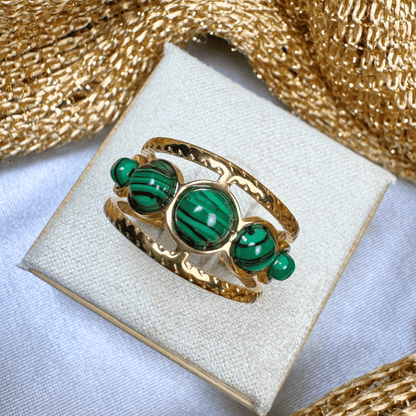 Gold ring with green gemstones on a white cushion with gold fabric background
