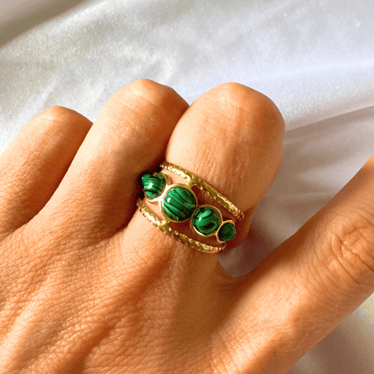 Gold ring with green gemstones on a hand against a white background