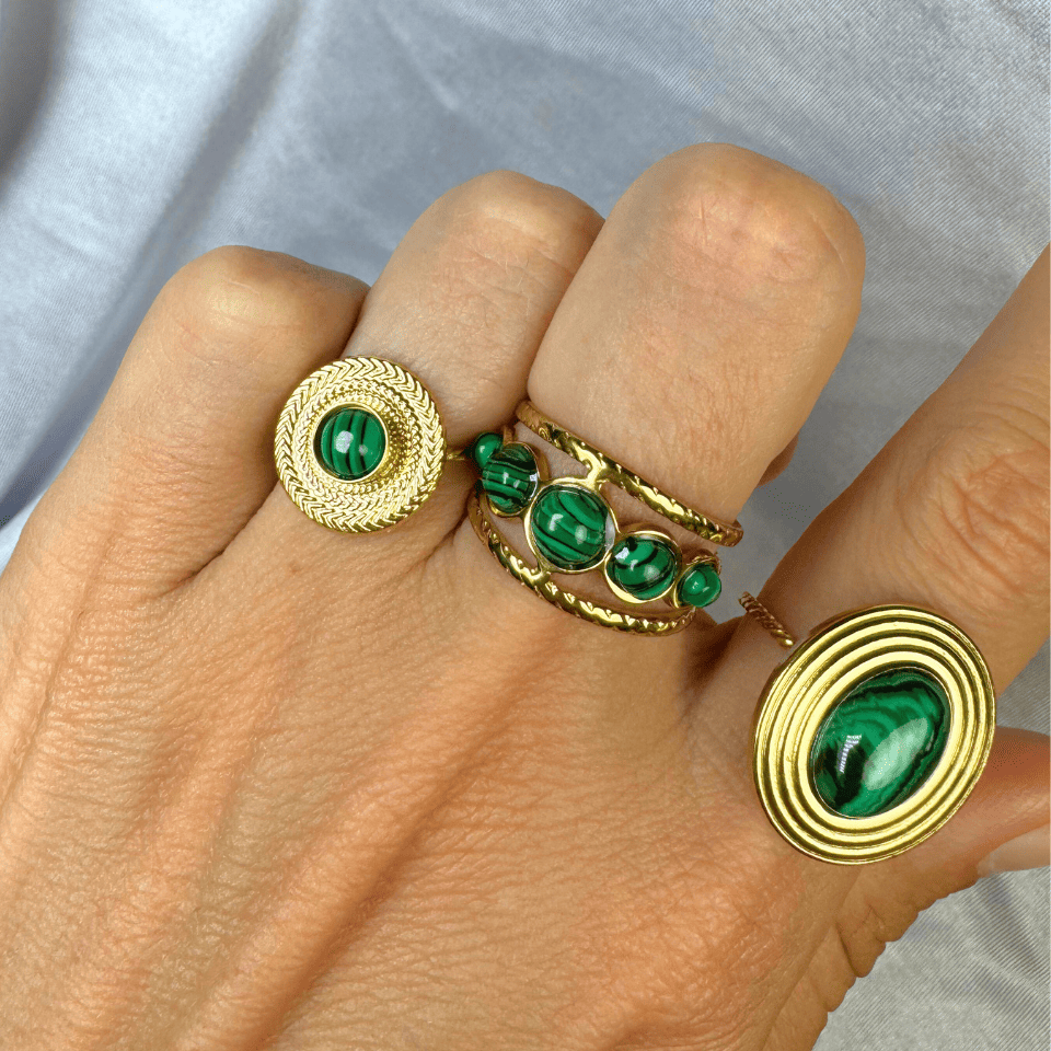 Gold rings with green gemstones on a hand against a light gray background
