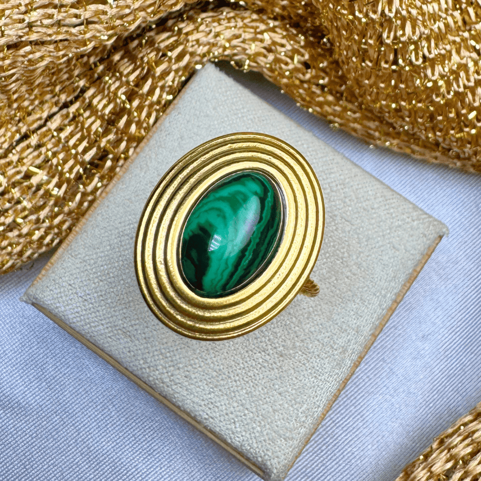 Gold brooch with green gemstone on a beige cushion, gold ribbon in the background