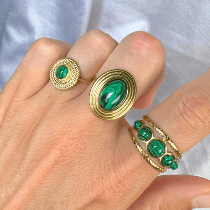 Gold rings with green gemstones on a hand against a light background