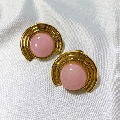Pair of earrings with pink round stones and gold circular designs on a white fabric background
