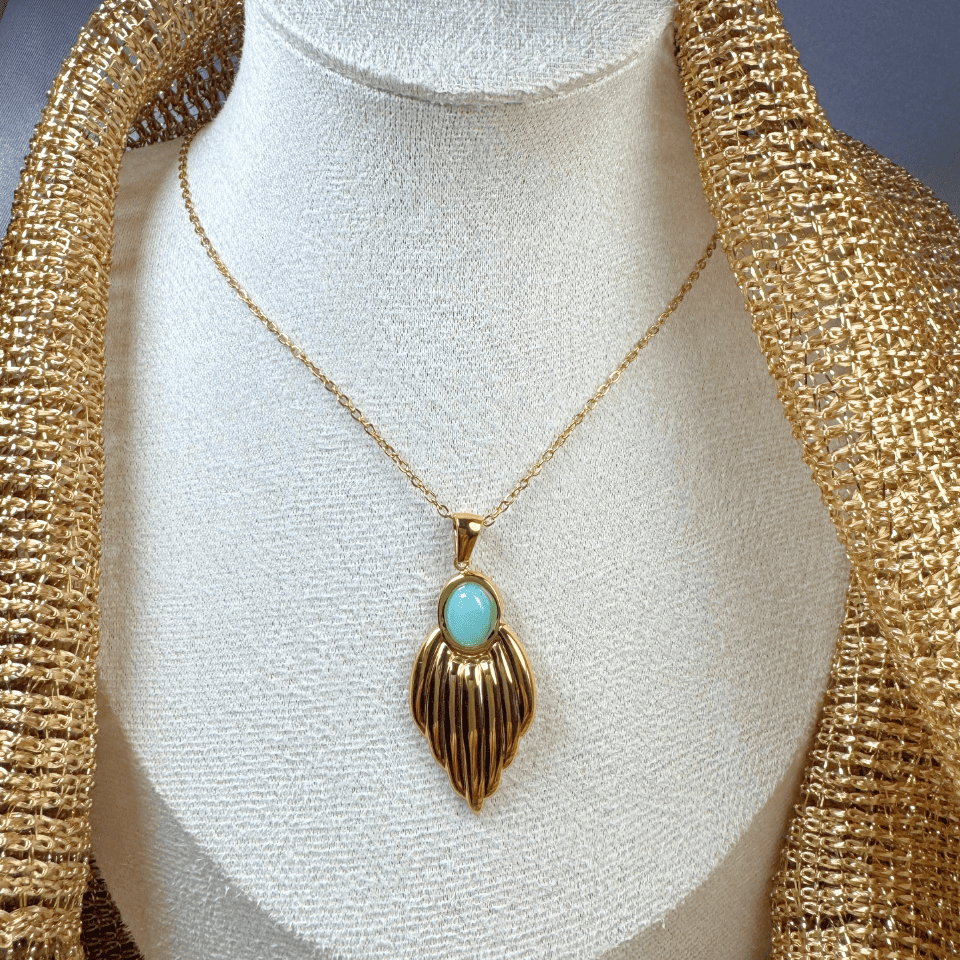 Gold necklace with a turquoise pendant on a mannequin bust.