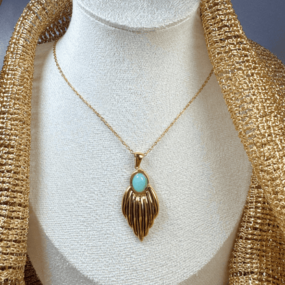 Gold necklace with a turquoise pendant on a mannequin bust.