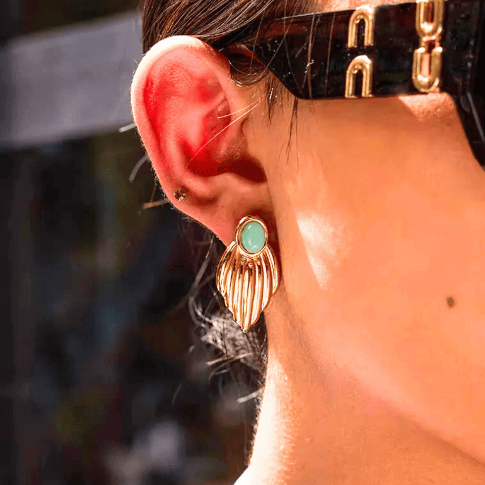 Close-up of an ear wearing a gold earring with a green gemstone, blurred background