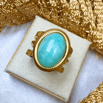 Gold ring with a turquoise stone on a white cushion with gold fabric background