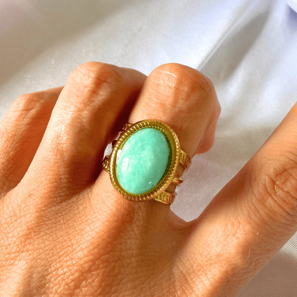 Turquoise ring with gold setting on a hand against a white background