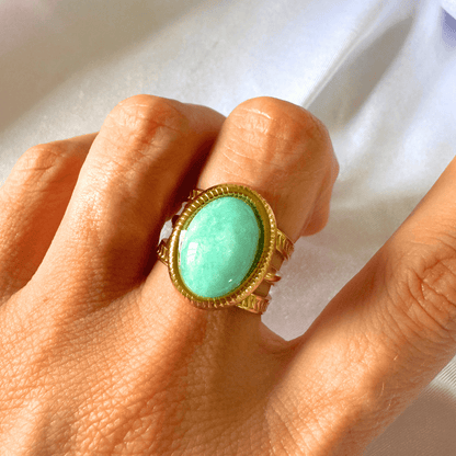 Turquoise ring with gold setting on a hand against a white background