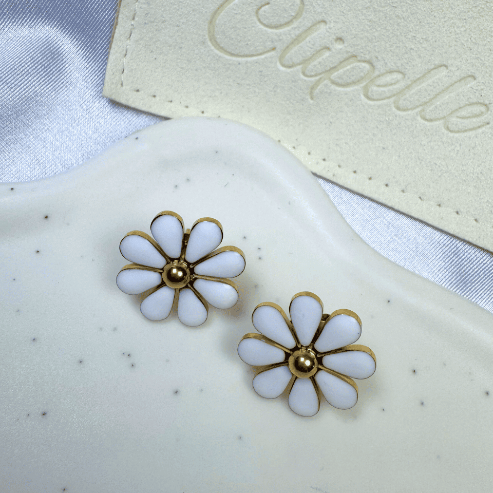 White flower-shaped earrings with gold centers on a white surface with 'Elipelle' branding.
