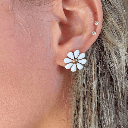 Close-up of an ear wearing a white flower-shaped earring with gold center.