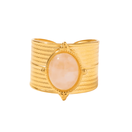 Gold cuff bracelet with a central peach-colored stone on a white background