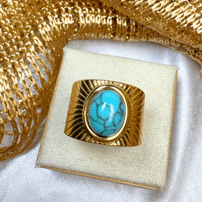 Gold ring with turquoise stone on a white cushion, gold decorative background