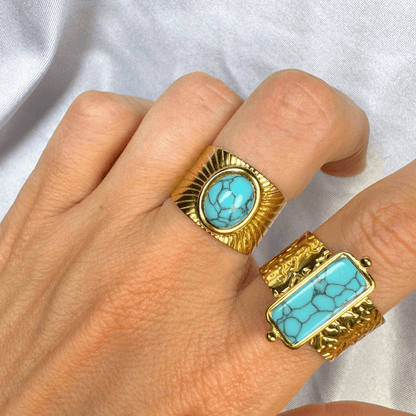 Gold rings with turquoise stones on a hand against a white background
