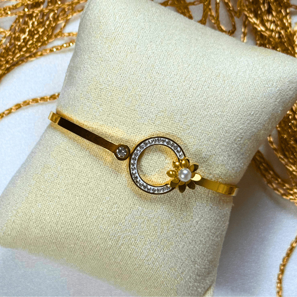 Gold bracelet with a pearl and gemstone design on a white cushion