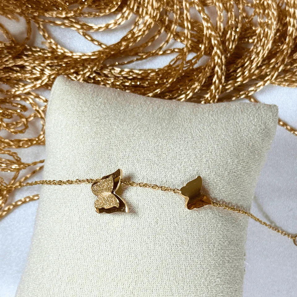 Gold butterfly bracelet on a white pillow with gold decorative background