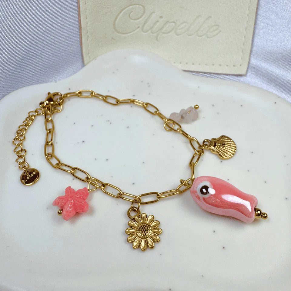 Gold bracelet with pink and gold charms on a white surface, with 'Clipelle' branding in the background.