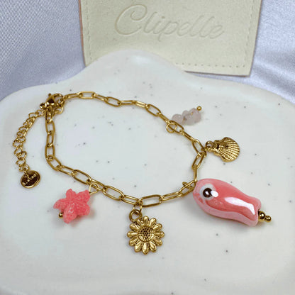 Gold bracelet with pink and gold charms on a white surface, with 'Clipelle' branding in the background.