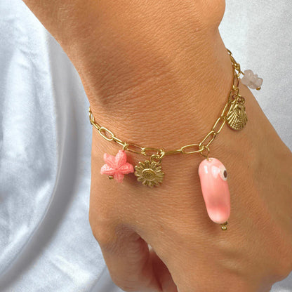 Gold bracelet with pink charms on a wrist against a white background