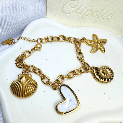 Gold bracelet with heart, shell, and starfish charms on a white dish with 'Clipelle' branding.