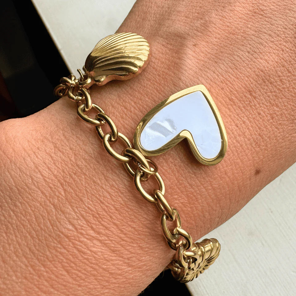 Gold bracelet with heart-shaped charm on a wrist against a neutral background