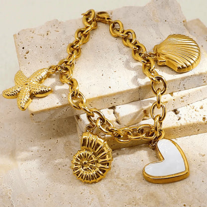 Gold charm bracelet with various charms on a beige stone surface