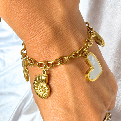 Gold bracelet with heart and shell charms on a wrist against a white background
