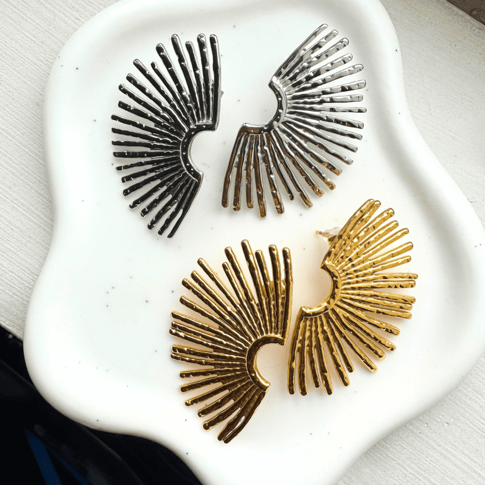 Pair of gold and silver sunburst earrings on a white stone surface.
