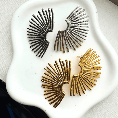 Pair of gold and silver sunburst earrings on a white stone surface.