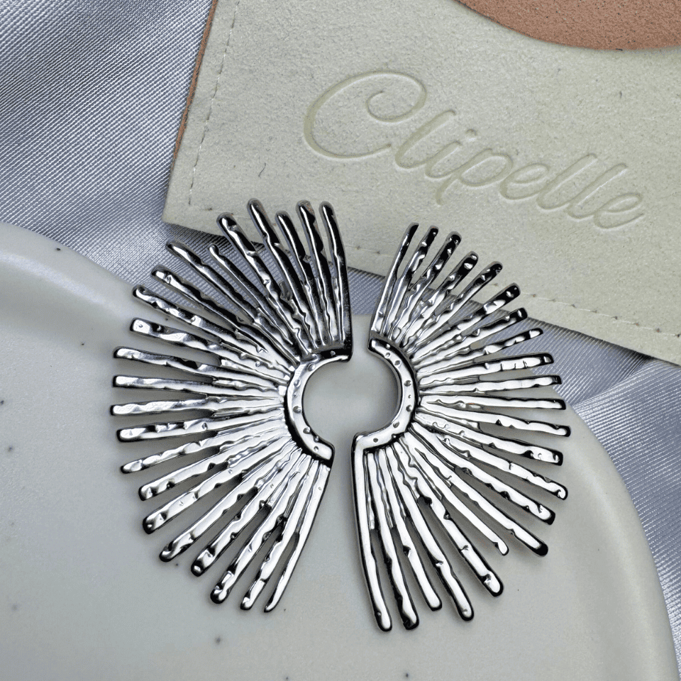Silver hair clip on a gray fabric background with 'Elipelle' branding.
