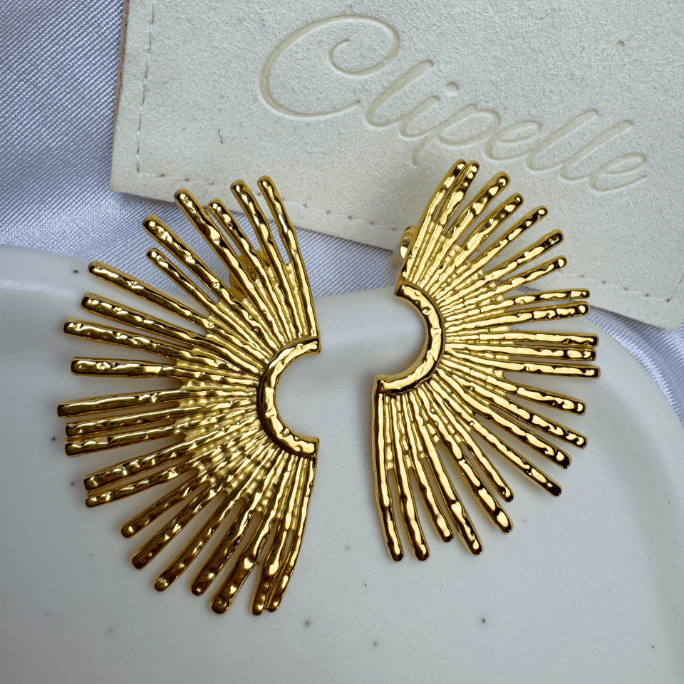 Gold sunburst earrings on a white card with 'Clipelle' branding.