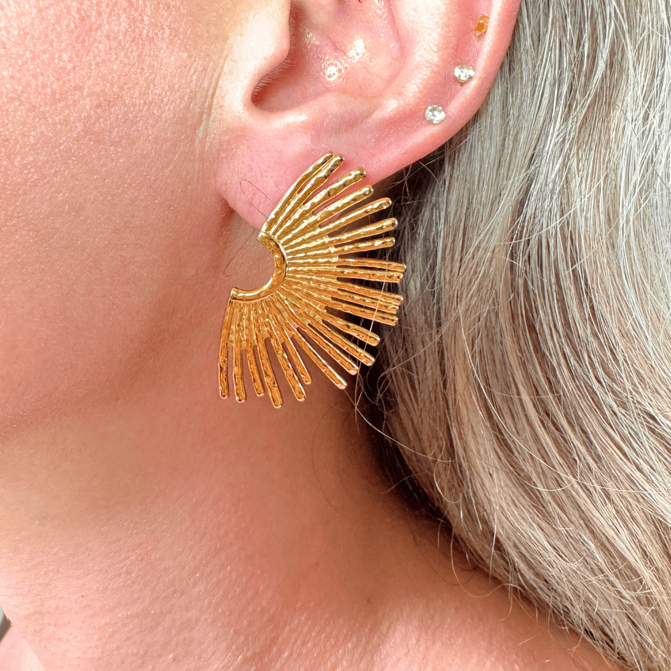 Gold earrings worn by a person with gray hair